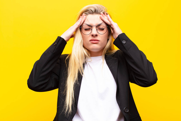 young pretty blonde woman looking stressed and frustrated, working under pressure with a headache and troubled with problems against yellow wall - Fotó, kép