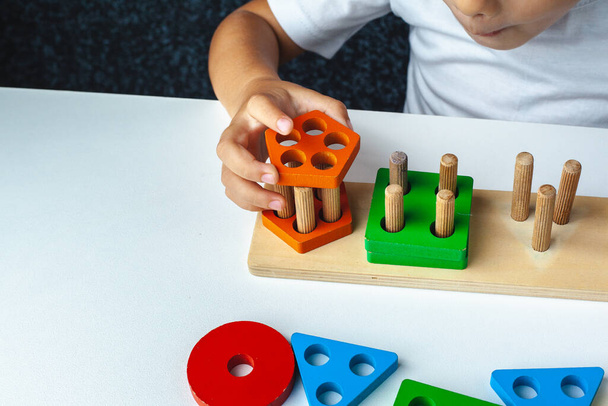 Child plays Montessori game. Kid collects wooden toy sorter. Multicolored geometric shapes, circle, square, triangle, rectangle. - Foto, Imagem