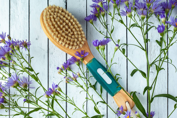 Anti-cellulite body brush with flowers lies on the background of boards. Body spa - Fotoğraf, Görsel