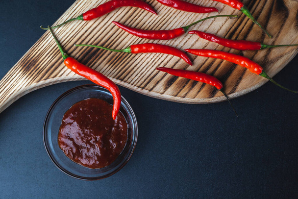 Pimienta roja caliente se encuentra en la tabla de cortar sobre fondo negro. salsa picante de pimiento rojo pimentón - Foto, Imagen