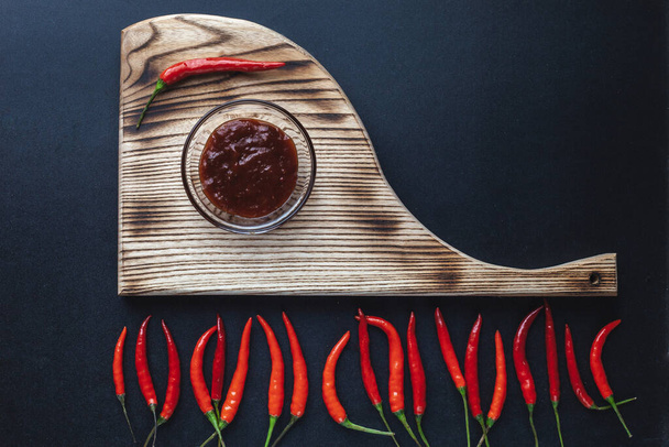 Горячий красный перец лежит на разделочной доске на черном фоне. острый соус паприка из красного перца. Тайская традиционная еда - Фото, изображение