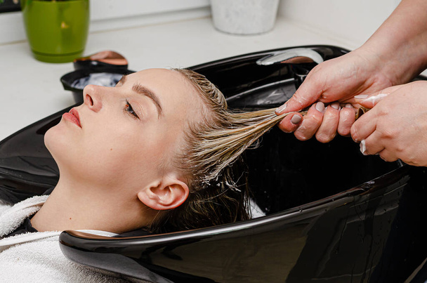 Coiffeur appliquant un traitement de mât sur cheveux mouillés dans un lavabo
. - Photo, image