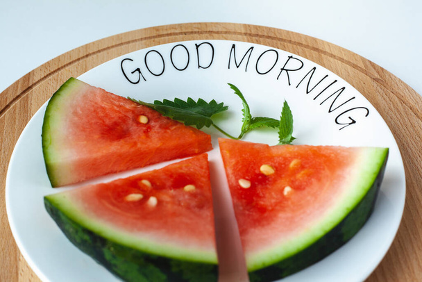 Wassermelone liegt auf einem Teller mit der Aufschrift Guten Morgen, auf einem Holztablett. Super Essen für Vegetarier. Geeignet für Banner, Plakate, Webseiten, Werbung. - Foto, Bild
