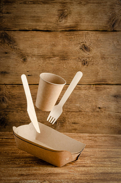 Flying disposable paper tableware on wooden background. Environmental care concept. Copy space. - Photo, Image