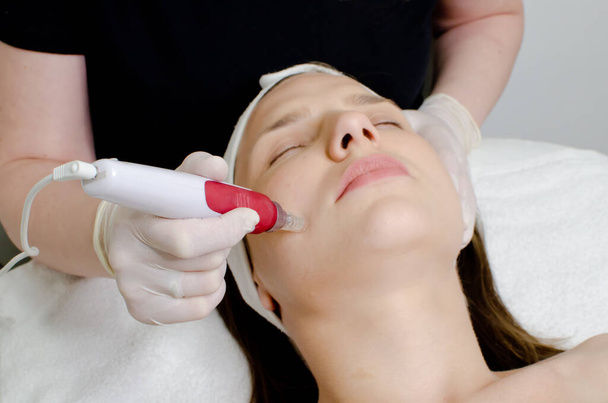 Kosmetolog, kosmetyczka w białych rękawiczkach stosująca pielęgnację skóry twarzy na twarzy młodej dziewczyny w salonie kosmetycznym.Kosmetologia i profesjonalna pielęgnacja skóry - Zdjęcie, obraz