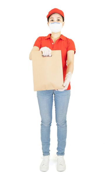 Delivery woman in red uniform isolated on white background.Courier in protective mask and medical gloves delivers takeaway food. Delivery service under quarantine, disease outbreak - Photo, image