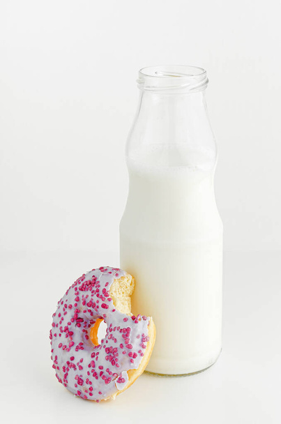 Delicious dessert. Milk bottle and fruit flavor doughnut with bite on white background. Vertical. - Foto, immagini