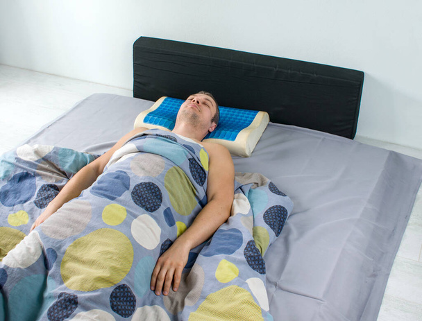 Miehet makaavat sängyllä ortopedisen tyynyn kanssa. Terve ryhti käsite. Latex tyyny muisti vaahto vaikutus, hydro geeli kerros. Lääketieteellinen hoito tyyny nukkua pään alla syvennys kaulan alla. - Valokuva, kuva
