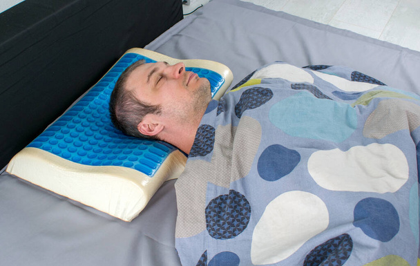 Férfiak fekszenek az ágyon ortopéd párnával. Egészséges testtartás koncepció. Latex párna memória hab hatással, hidro zselé réteg. Orvosi kezelés párna aludni a fej alatt egy szünet a nyak alatt. - Fotó, kép