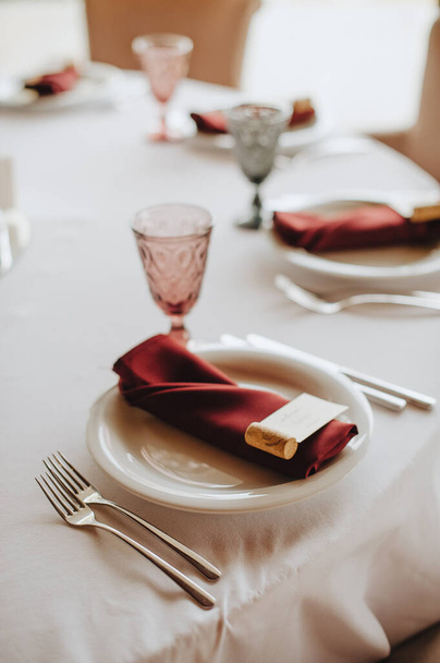 De tafel is bedekt met een wit tafelkleed, geserveerd. Borden, bestek, servet, roze bril, zitkaarten, takje groen. - Foto, afbeelding