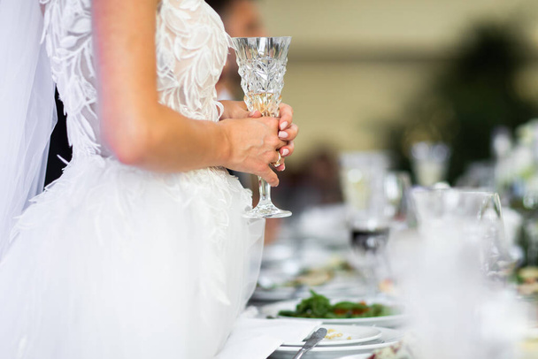 The bride is standing at the table and holding a glass. - Foto, afbeelding