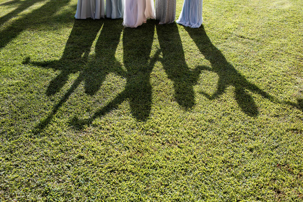 Schaduwen van meisjes in jurken op het gras. Je kunt zien hoe ze met hun handen zwaaien.. - Foto, afbeelding