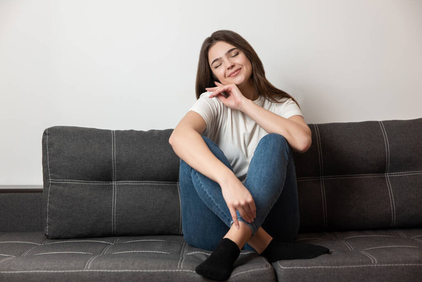 young beautiful brunette woman sitting on the sofa in her appartment looking positive, feels cozy at home. - Fotografie, Obrázek