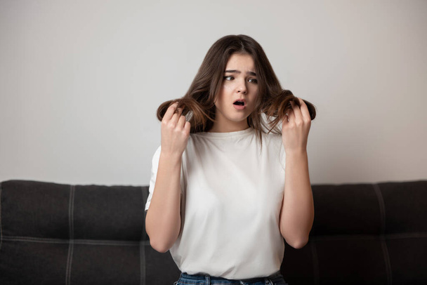brunette young woman with damaged long hair and split ends looks desparate and unhappy with her hairstyle, bad hair day concept. - Foto, imagen