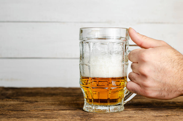 Male hand holding a half full beer glass with foam on wooden table. Copy space - Foto, imagen