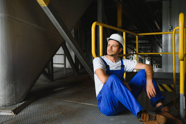 Smiling and happy employee. Industrial worker indoors in factory. Young technician with white hard hat. - Foto, Imagem