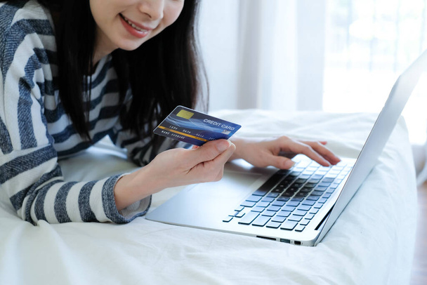 寝室でオンラインショッピングのためのクレジットカードとラップトップを使用してアジアの女性. - 写真・画像