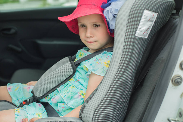 Un bambino con un cappello rosso è seduto in un'auto nel seggiolino di un bambino
 - Foto, immagini
