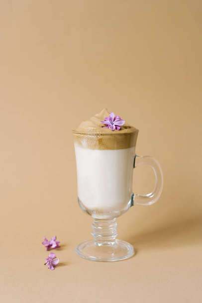 Beautiful dalgon coffee drink with foam in a transparent Cup and lilac flowers on a beige background. Copy space - Fotografie, Obrázek