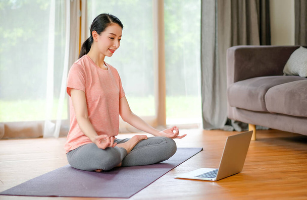 Schöne Frauen, die Yoga mit unterschiedlicher Körperhaltung und Blick Beispiel aus Laptop auch sie glücklich aussehen und entspannen. Konzept des Trainings zu Hause für eine gute Gesundheit und Verhinderung einer Virusinfektion durch Pandemie. - Foto, Bild