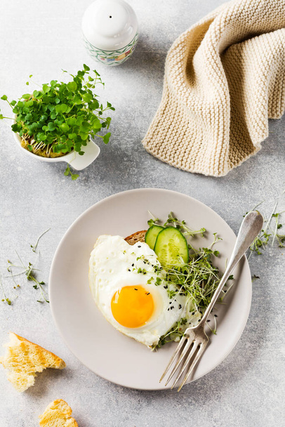 Traditional English breakfast with fried eggs with arugula microgreen in gray ceramic plate on gray concrete old background. Top view. - Fotografie, Obrázek
