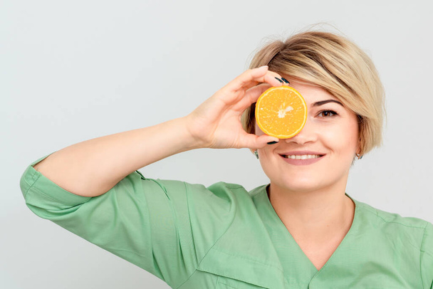 Cosmetologist is having piece of orange closing one eye isolated on white background. - Photo, Image