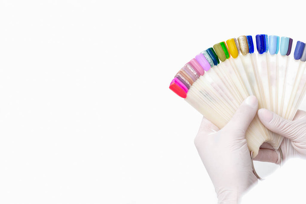 Μανικιουρίστα χέρια κατέχουν μανικιούρ παλέτα χρωμάτων νυχιών σε λευκό φόντο. - Φωτογραφία, εικόνα