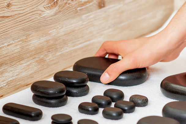 Manos de masajistas tomando piedras negras de masaje caliente de conjunto sobre la mesa en el spa
. - Foto, Imagen