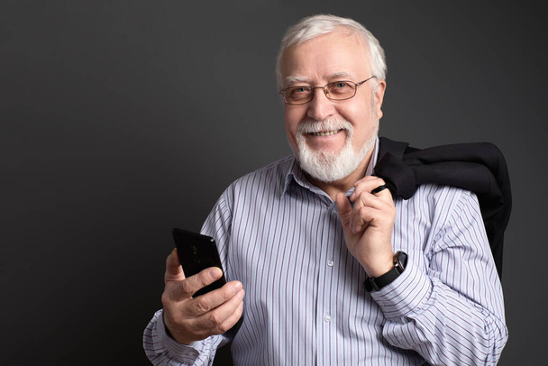 homme aux cheveux blancs, aux lunettes avec un téléphone sur un fond gris sourit amical
 - Photo, image