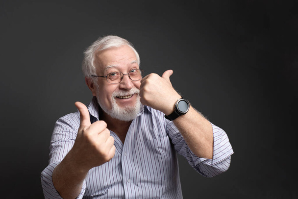negocios, hombre de pelo blanco en gafas sobre un fondo gris sonríe y muestra aprobación
 - Foto, imagen