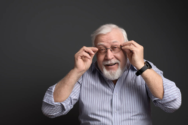 carismático, hombre de pelo gris sostiene sus gafas y sonríe
 - Foto, imagen