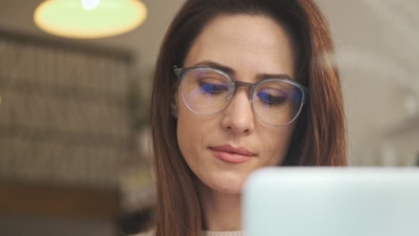 A close-up view of a calm young woman wearing glasses is working in the cafe indoors - Séquence, vidéo