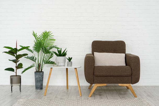 Moderní obývací pokoj v moderním domě s pohodlným křeslem, polstrovaným nábytkem, koberec na podlaze, dřevěný trojúhelníkový stůl, zelený domeček v květináči proti cihlově bílé zdi s kopírovacím prostorem - Fotografie, Obrázek