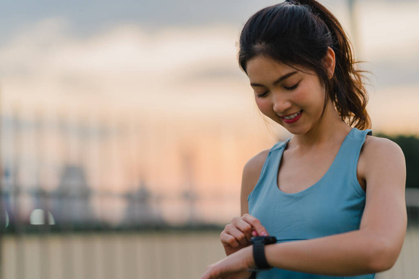 Young Asia athlete lady exercises checking progress looking heart rate monitor on smartwatch in urban city. Teen girl runner resting exhausted after intense running workout training cardio in morning. - Photo, Image