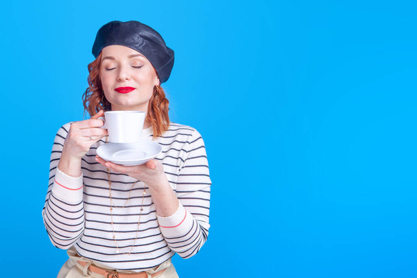 γυναίκα με ένα φλιτζάνι καφέ ή τσάι στο στούντιο σε μπλε φόντο - Φωτογραφία, εικόνα