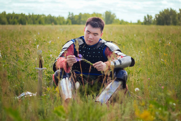 A medieval Asian warrior sits in a field in tall grass. - Фото, изображение