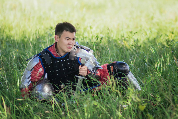 A medieval Asian warrior in armor is resting while sitting in tall grass. - Фото, изображение