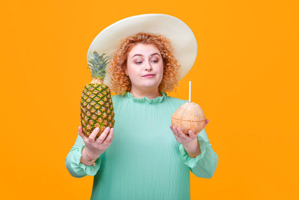 Blonde Frau mit Ananas und Kokosnuss in den Händen auf gelbem Hintergrund im Studio - Foto, Bild