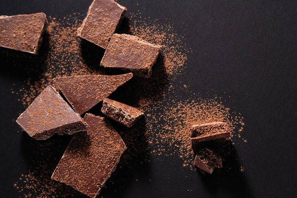 gebrochener Schokoladenriegel auf schwarzem Hintergrund - Foto, Bild