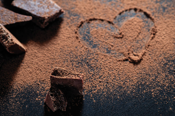broken chocolate bar on a black background, cocoa powder painted heart - Foto, immagini