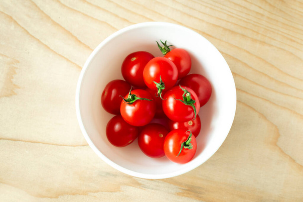 Red cherry tomatoes in a small white bowl on a wooden Board - Fotó, kép