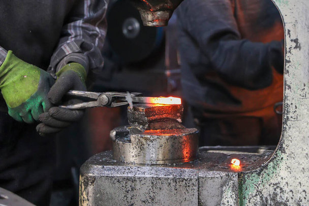 Blacksmith käsittelee kuumaa metalliesinettä alasimella työpajassa. Blacksmithin työprosessi. Taonta rauta sauva alasin. - Valokuva, kuva