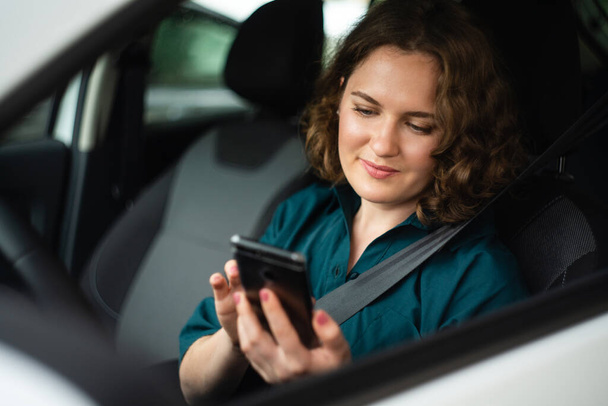 Woman driver sitting in car and looking at smartphone screen - Фото, изображение