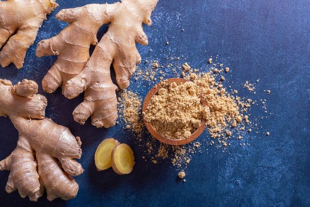 Ginger powder in a wood bowl and ginger root with a blue background - Foto, Imagem
