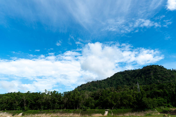 Hegyek bőséges fákkal és van egy nagyfeszültségű villanypózna. A kék ég és a fehér felhők alatt. - Fotó, kép
