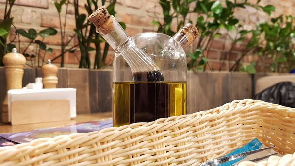 Glass bottle with sauce and butter for pizza and pasta, standing on a served wooden table in an Italian restaurant with brick walls and green plants - Photo, Image