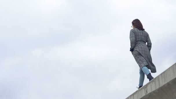 A young woman walks on a concrete fence. Girl wearing a coat - Foto, Imagen