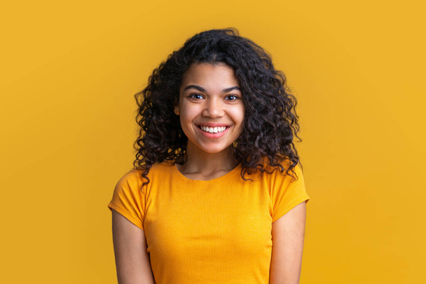 Portrait of young attractive african american woman on bright background. Cute girl with voluminous curly hair looking happy with wide perfect smile on her face. - 写真・画像