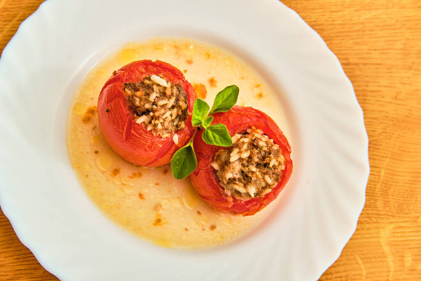 Lekkere rode gevulde tomaten met rijst en gehakt vlees op witte plaat op houten tafelblad uitzicht - Foto, afbeelding