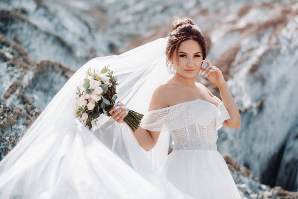 Beautiful bride in a wedding dress with a bouquet on the top of the salt mountains. A stunning young bride with curly hair . Wedding day. . Beautiful portrait of the bride without the groom - Valokuva, kuva